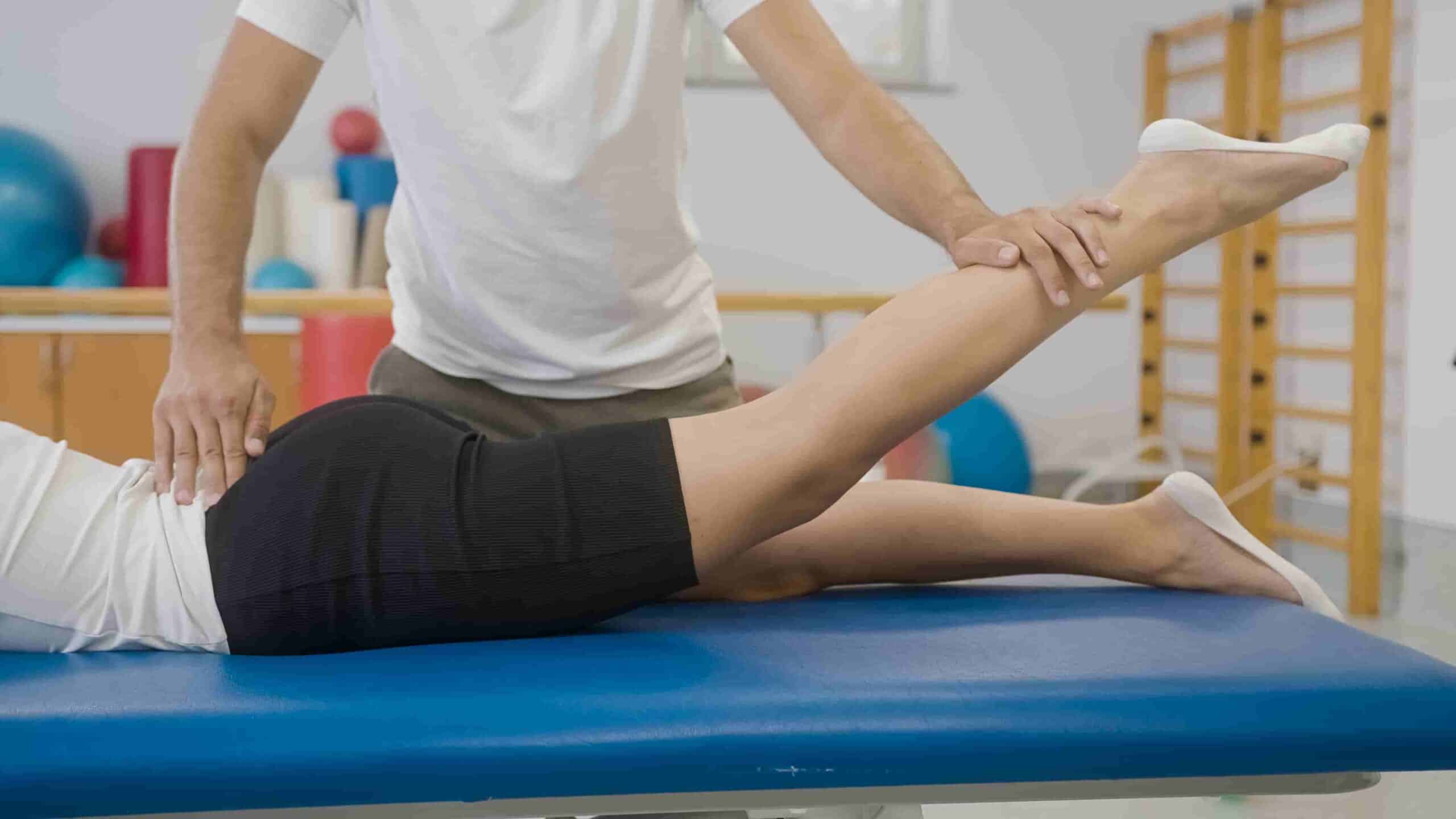 Physical therapist assisting a patient with a leg stretch during a rehabilitation session on a treatment table.